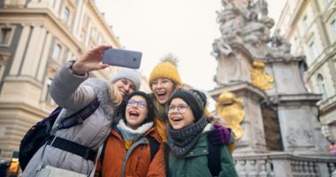 Family bundled up in winter coats and hats take a selfie in a European city square