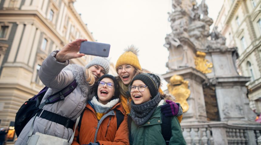 Family bundled up in winter coats and hats take a selfie in a European city square