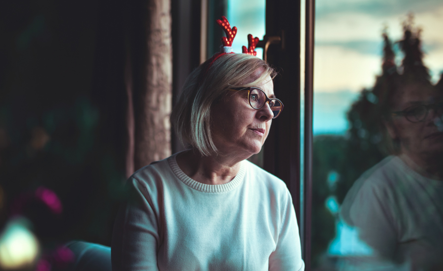 woman wearing a festive reindeer antler headband looks out of the window, a wistful, sad expression on her face