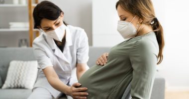 Midwife examines the belly of a pregnant patient, both are sitting on couch, not exam room