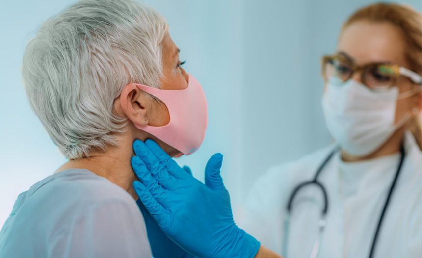 doctor wearing face mask and hand gloves feels the sides of a female patient's neck