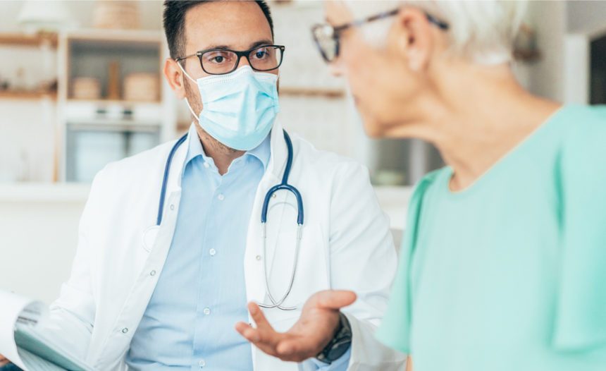 provider wearing a surgical mask sits next to older patient, the two in discussion