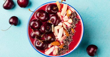 overhead view of smoothie bowl with cherries, apple slices, and seeds decoratively arranged on top