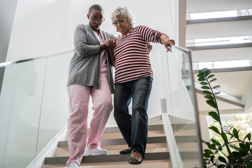 Female provider/caretaker helps an elderly female patient down some stairs