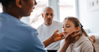 provider checks neck of pediatric patient while parent watches