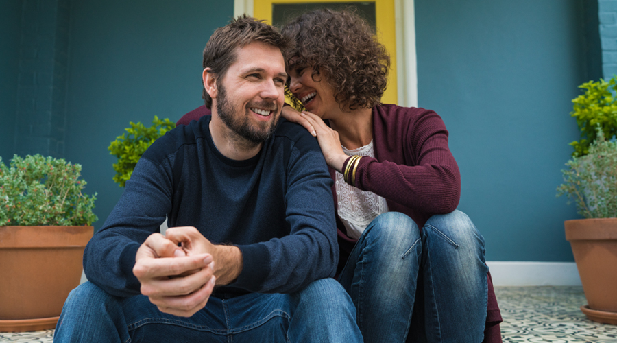 Young male/female couple sit on front steps of house, laughing and talking