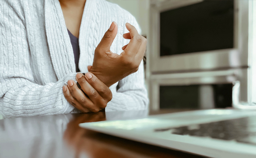 close-up shot of a woman holding her wrist in pain, a laptop in the foreground of the photo