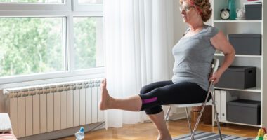woman wearing exercise clothing sits in chair doing a leg exercise