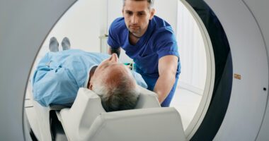 Male health provider helps a older male patient into a MRI machine