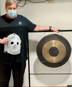 UNC health patient Brian Stepien with the custom face mask he wore during treatment, standing next to the end-of-treatment gong