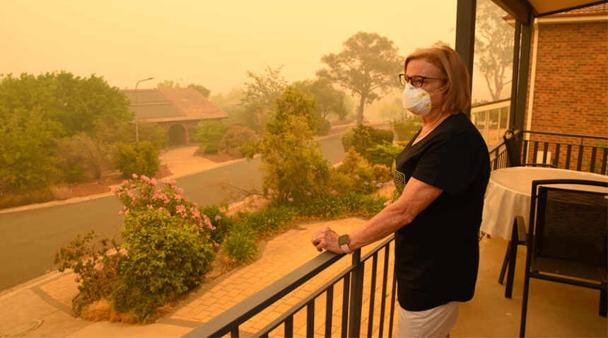 A woman, on a balcony, wears a face mask to protect herself against very dangerous level of air pollution. A thick yellow fog coming from the nearby forest fires can be seen
