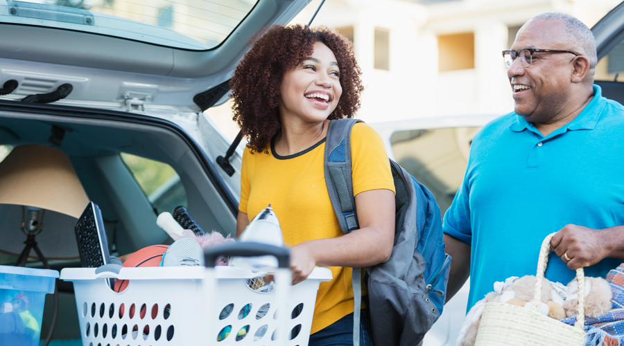 college-aged girl carries a laundry basket out of the trunk of a car while her dad carries a grocery bag