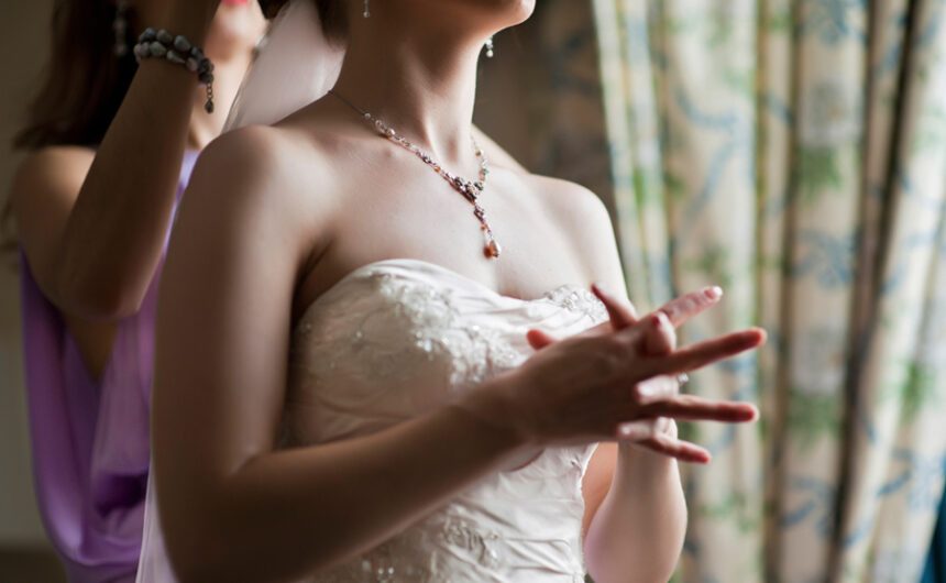 mid-view of bride wearing wedding dress, standing in front of a window in anticipation