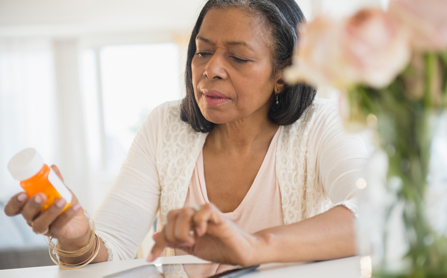 older woman sits at her kitchen table, analyzing the pill container in her hand