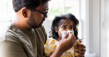 Father helps young daughter wipe her nose with a tissue