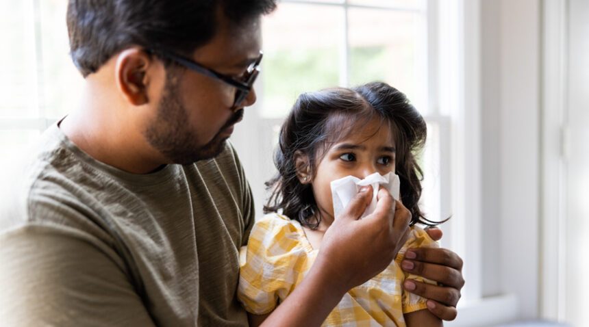 Father helps young daughter wipe her nose with a tissue
