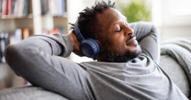 Man listening to music through headphones leans back on couch with hands behind his head, relaxing and enjoying the music