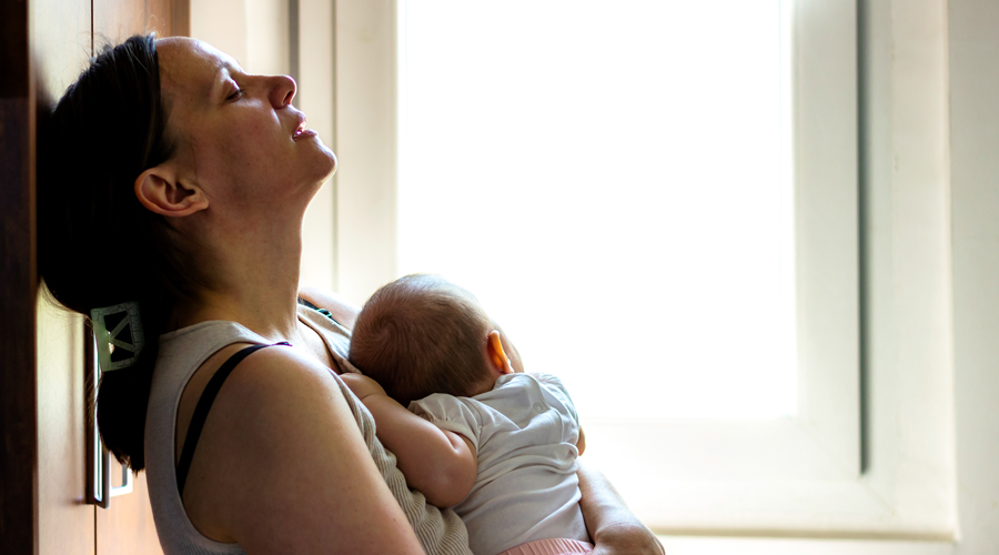 Mom leans head against wall in frustration while holding newborn baby