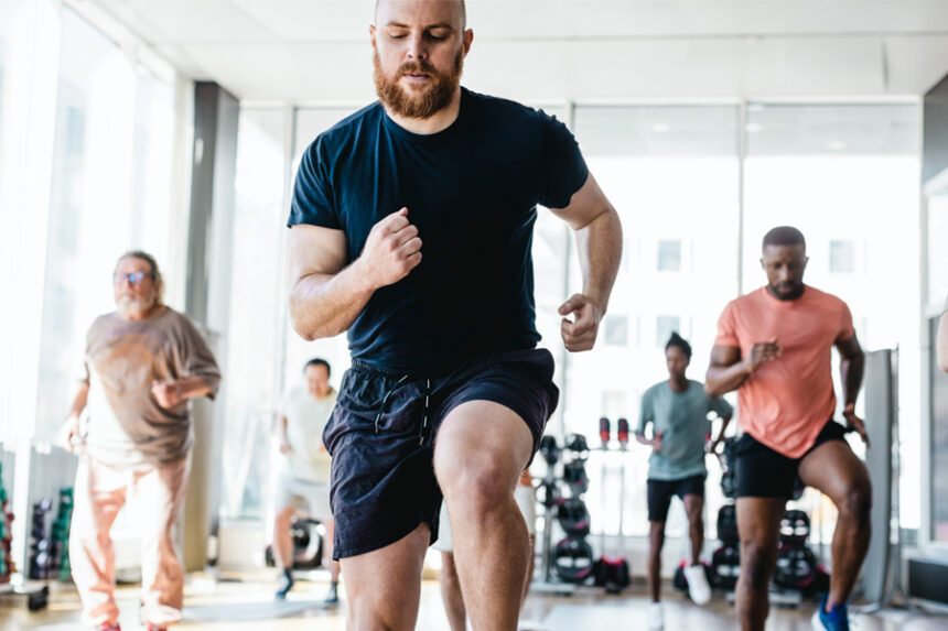 Image focused on a man running in place in a fitness class while others in the background do the same movement