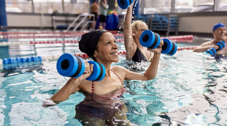 Senior woman does water aerobics with foam weights in an indoor pool