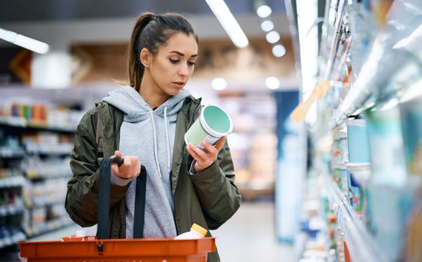 Sporty-looking woman looks at the label of a food item in the aisle of a grocery store