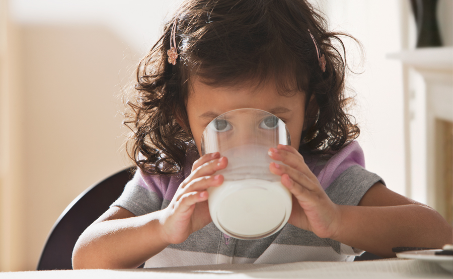 toddler girl drinks a glass of milk