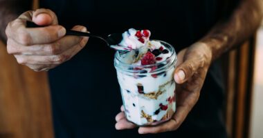 close-up view of someone talking a spoonful of a jar of vanilla yogurt topped with berries and granola
