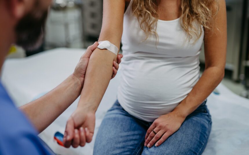 Pregnant woman in a exam room with bandage on her arm meant to indicate she has just had her blood drawn