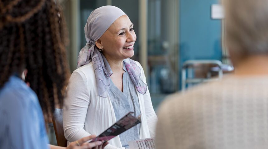 Woman wearing head scarf to cover bald head smiles while talking to providers