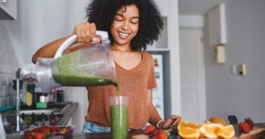 Smiling woman pours herself a green smoothie in an apartment kitchen