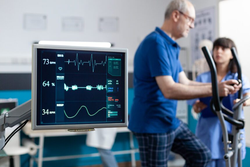 Older male patient uses elliptical machine in the background with EKG machine displayed in the foreground