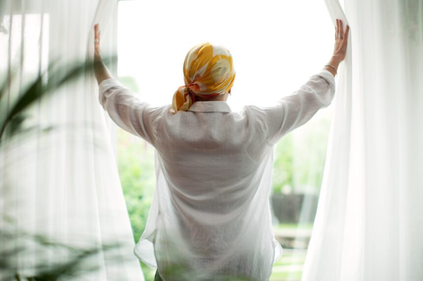 Woman wearing a head scarf opens the window curtains to look outside