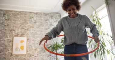 Smiling woman plays with a hula hoop in her living room