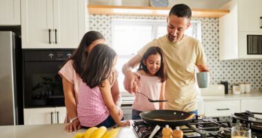 Family of mom, dad, and two girls make breakfast in their kitchen