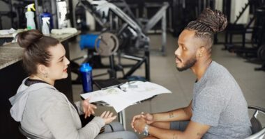 Woman dressed in workout clothes talks to her personal fitness trainer in a gym