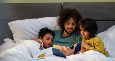 Dad reads a book to his two boys as they are all snuggled in bed