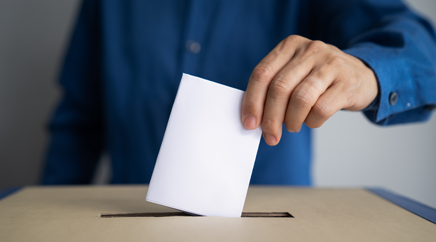 anonymous male figure placing a piece of paper in a ballot box