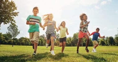 Children happily running on a grassy field, sun shining in the background