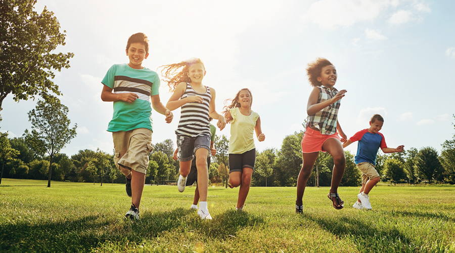 Children happily running on a grassy field, sun shining in the background