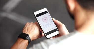 Man looking at his smartphone (smart watch on his arm) as he views a heart rate-tracking app