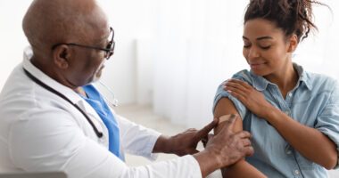 Doctor places a bandage on a patient's arm, to indicate she just got her flu shot