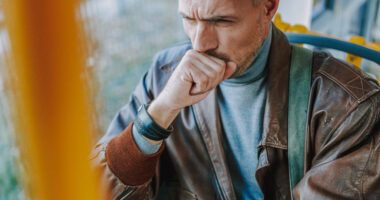 A man covers his mouth to block a cough, while he rides on a public transit bus