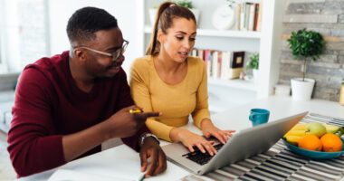 Young adult couple sits at counter looking at laptop together