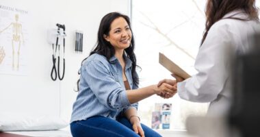 a woman sitting on an exam table shakes hands with a new provider