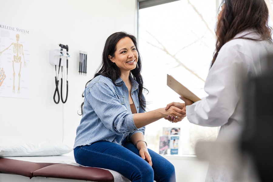 a woman sitting on an exam table shakes hands with a new provider