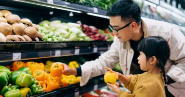 Dad and young daughter look at yellow peppers in the produce aisle of a grocery store