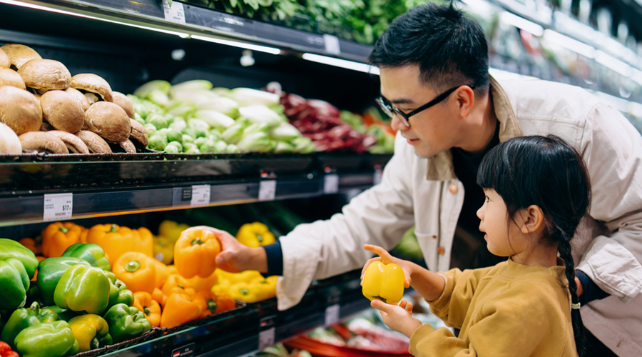 Dad and young daughter look at yellow peppers in the produce aisle of a grocery store