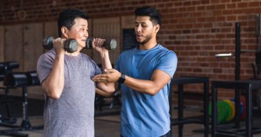 man lifts light dumbbells while a personal trainer guides him