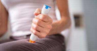 close-up view of woman pushing an EpiPen into her leg.