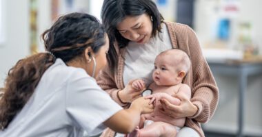 mom holds her infant in her lap while a provider listens to the baby's heart with a stethoscope